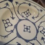 En Kahla Fattigmands muselmalet tallerken i hvid porcelæn med blåt mønster, set lidt fra oven med et fokus på dekorationerne.