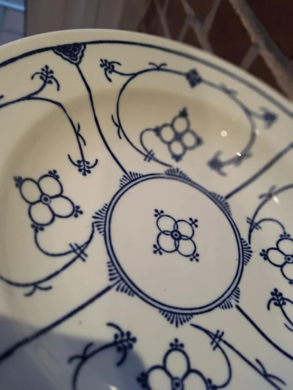 En Kahla Fattigmands muselmalet tallerken i hvid porcelæn med blåt mønster, set lidt fra oven med et fokus på dekorationerne.