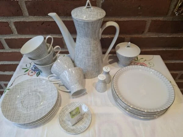 Et stort Rosenthal kaffeservice i hvid porcelæn med et gråt, flettet grafisk mønster. Inkluderer kaffekande, kopper, underkopper, tallerkener, sukkerskål og salt/peberbøsser.