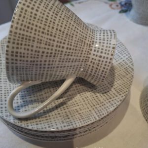 En Rosenthal kaffekop i hvid porcelæn med gråt grafisk mønster, lagt ned på en stak underkopper. Chippen er synlig på koppen.