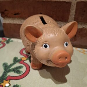 En charmerende terracotta sparegris med et venligt ansigt og sort øjne, stående på en juledug.