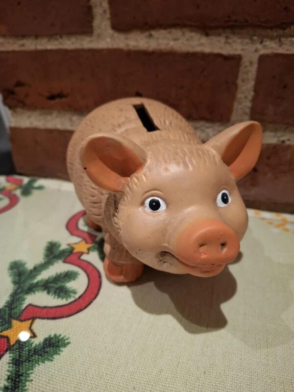 En charmerende terracotta sparegris med et venligt ansigt og sort øjne, stående på en juledug.