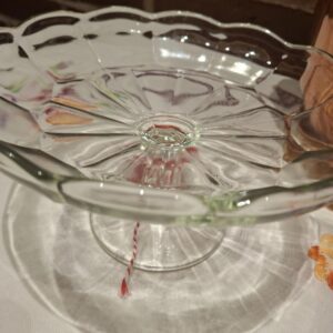 Et tomt glas opsatsfad med en bølget kant og mønstret bund, stående på en hvid dug, set fra siden.