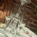 Et slankt champagneglas står vendt på hovedet foran to stående glas; den dekorative stilk og runde fod ses tydeligt.