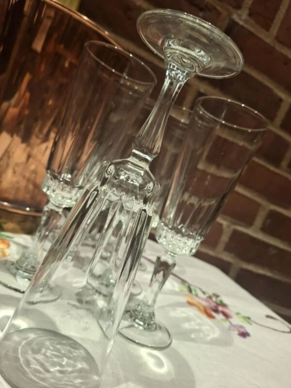 Et slankt champagneglas står vendt på hovedet foran to stående glas; den dekorative stilk og runde fod ses tydeligt.