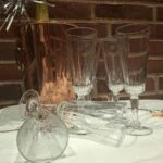 Slanke champagneglas står og ligger på en hvid dug foran en kobberfarvet køler og en murstensvæg.