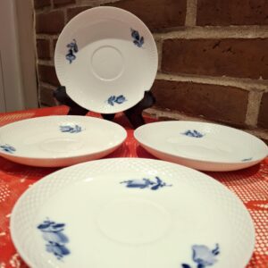 Fire hvide Royal Copenhagen Blå Blomst underkopper, 16 cm, med blå blomster og musselmønster, på rød dug.