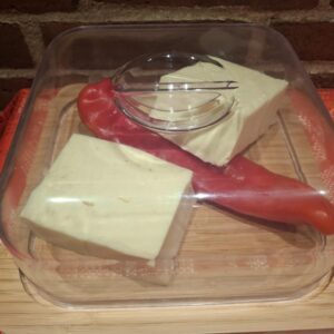 Rundt bambus kage- og ostefad med klart akryllåg. Indeni ligger to stykker hvid ost og et rødt peberfrugt.