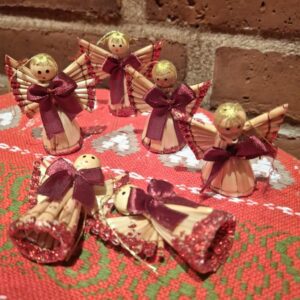 Seks juleengle lavet af lyst fletværk med bordeaux sløjfer og glimmer, liggende på en rød dug.