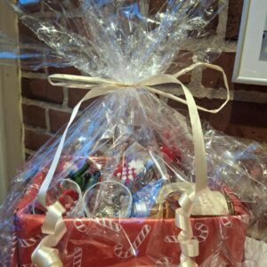 En indpakket julegavekurv med rød julepapir og en beige sløjfe. Indholdet skimtes igennem klar folie.