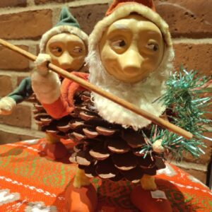 To håndlavede koglenisser med papsansigter, kvastskæg, nissehuer. En har en tynd pind og en julekrans i hånden.