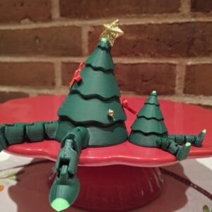 To grønne 3D-printede juletræer med bevægelige ben og julepynt, det ene et større, det andet mindre, stående på en rød kageopsats.
