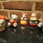 Fem musselmalede keramikfigurer forestiller en musefamilie i forskellige juleoutfits og positurer, på sort baggrund.