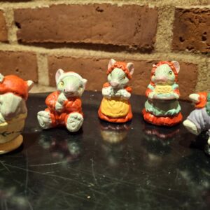 Fem musselmalede keramikfigurer forestiller en musefamilie i forskellige juleoutfits og positurer, på sort baggrund.