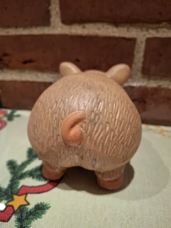 Bagsiden af en terracotta sparegris, der viser dens krøllede hale og teksturerede overflade. På juledug.