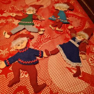 Fire håndlavede filtnisser i rød, grøn og blå, med broderede ansigter og perledetaljer, liggende på rød dug.