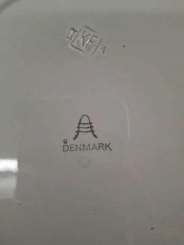 Bagsiden af en hvid Aluminia fajancetallerken, der tydeligt viser stemplet 'Aluminia Denmark' med et stillet A-logo.