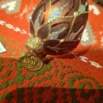 Nærbillede af kobberfarvet glasornament med glimmer, små klare pyntesten, metalhætte og oval mærkeplade med BRINK.