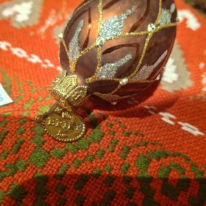 Et aflangt, hånddekoreret juleornament i kobber- og guldnuancer med glimmerede detaljer og diamanter.