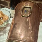 Nærbillede af champagnekølerens ringhåndtag og montering med nitter. Kobberfarvet side med ridser og messingfarvet kant.