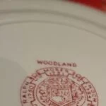 Nærbillede af bagsiden af en Woodland tallerken fra Wood & Sons med rødt stempel, der indikerer 'WOODLAND' og producentinformation.