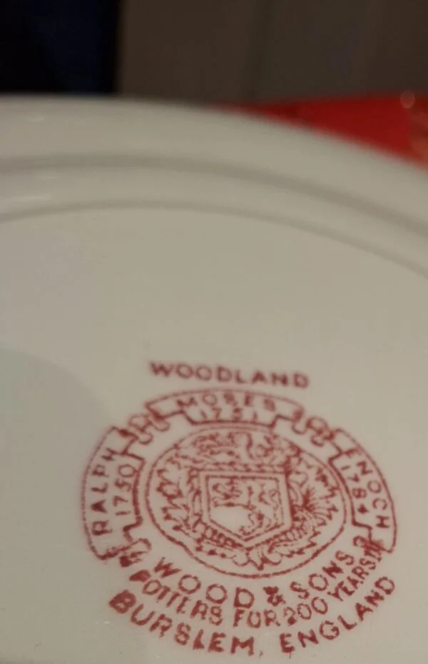 Nærbillede af bagsiden af en Woodland tallerken fra Wood & Sons med rødt stempel, der indikerer 'WOODLAND' og producentinformation.