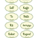 Nærbillede af 10 ovale, cremefarvede køkkenklistermærker med grøn kant til krukker, med teksten 'Mel', 'Sukker', 'Salt', 'Kaffe', 'Te', 'Pasta', 'Ris', 'Havregryn', 'Kakao' og 'Rugmel' på dansk.
