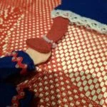 Nærbillede af ben og tøj på en håndlavet filtnisse. Hvid blonde og små perler ses på tøjet.