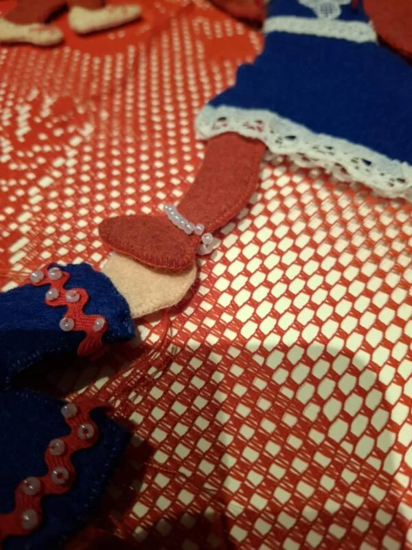 Nærbillede af ben og tøj på en håndlavet filtnisse. Hvid blonde og små perler ses på tøjet.