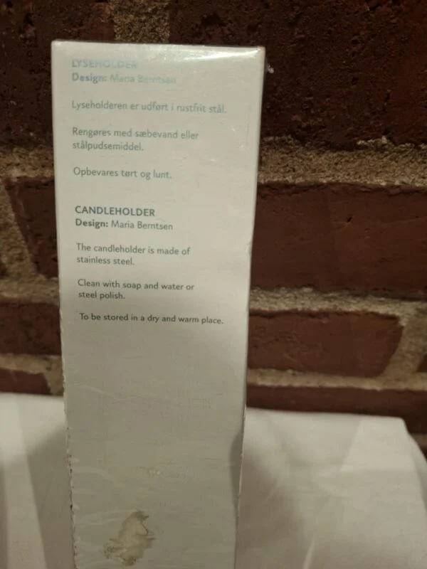 Bagsiden af Georg Jensen lyseholderen 'Christmas Nordica's æske, med produktinformation på dansk og engelsk om design og materiale.
