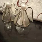 To engle med gennemsigtige glasfelter, metalrammer, vinger og lyse runde hoveder på et mørkt underlag.