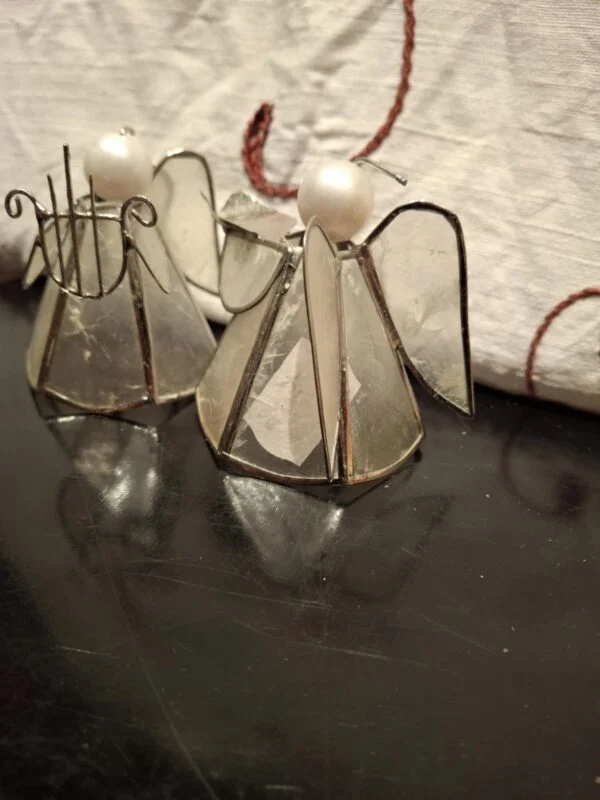 To engle med gennemsigtige glasfelter, metalrammer, vinger og lyse runde hoveder på et mørkt underlag.