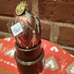 Ægformet BRINK glasornament med kobberfarve og glimmer vist oprejst i en mørk holder.