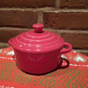 En lille rød stentøjsgryde med låg fra mærket Ernesto, placeret på en rød og grøn juledug.