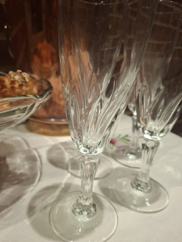 Nærbillede af en champagnefløjtes snoede mønster, dekorative stilk og runde fod; et andet glas står bagved.