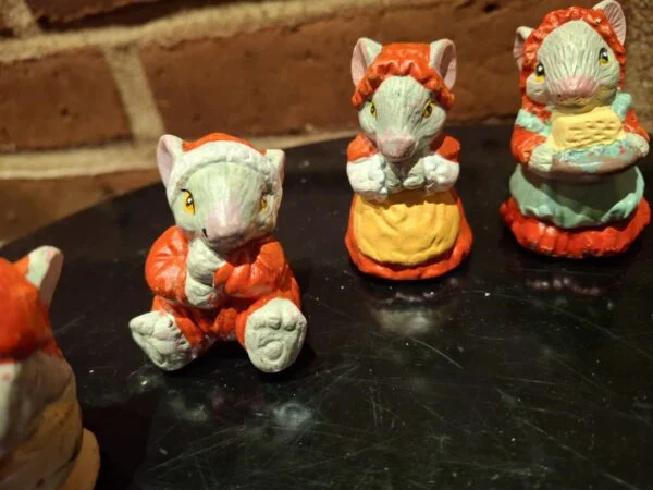 Nærbillede af to musselmalede keramikmusefigurer. Den ene mus bærer rød frakke og den anden sover i en gul kop.