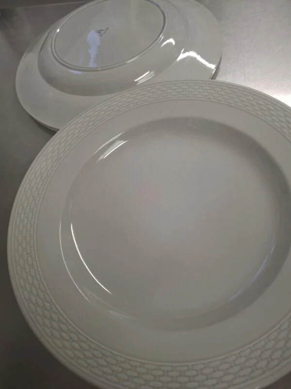 To hvide Aluminia tallerkener med en flettet kant, den ene ovenpå den anden, på en reflekterende overflade.