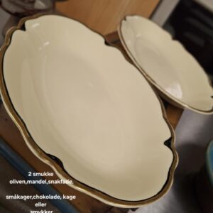 To elegante, ovale snackfade i cremefarvet porcelæn fra Johnson Bros. 'Victorian' stil, med guld- og mørkeblå kant. Teksten '2 smukke oliven,mandel,snakfade. småkager,chokolade, kage eller smykker virtorian johnson bros England' er på billedet.