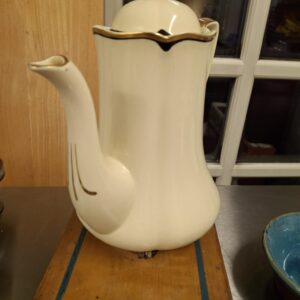 En slank, cremefarvet kande fra Johnson Bros. 'Virtorian' med guldkant og en elegant sort stribe, stående på en træoverflade. Kanden har et unikt designet tud og låg.