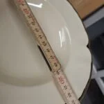 Udsnit af en cremefarvet dyb tallerken med mørk og guldfarvet kant samt en målestok; hele målingens start er ikke synlig.