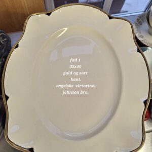 Stort, ovalt cremefarvet fad fra Johnson Bros. (Victorian) med en elegant guld- og sort kant. Teksten 'fad 1 33x40 guld og sort kant. engelske virtorian. johnson bro.' er synlig på fadets overflade.