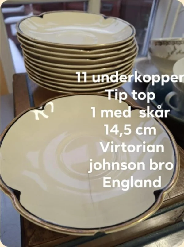 En enkelt cremehvid Johnson Bros. 'Victorian' underkop med guldkant, der er placeret foran en stabel lignende underkopper. Der er tekst på billedet, der angiver antal, mål og mærke, samt info om et skår.