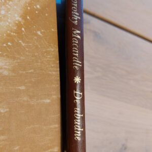 Bogryg af Dorothy Macardles "De ubudne" med guldbogstaver på mørkebrun ryg