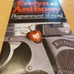Forside 'Programmeret til mord' med hjertevedhæng og pistol