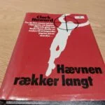 Rødt omslag med silhuet og titel 'Hævnen rækker langt'