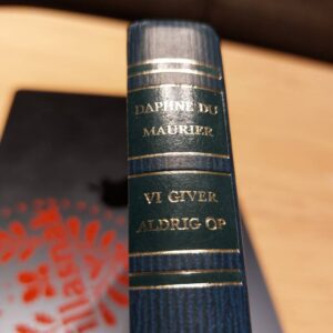 Bogryg af 'Vi giver aldrig op' af Daphne du Maurier i mørkeblå med guldbogstaver