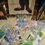Små glas på fod med gule, blå, grønne og rosa felter samlet på en mønstret bakke.