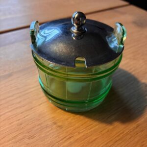 Grøn glasbeholder med sølvlåg på et træbord