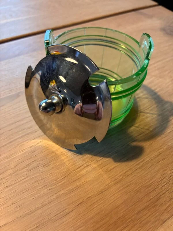 Åben grøn glasbeholder med skinnende sølvlåg på træbord