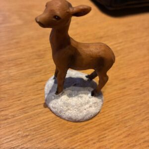 Lille brun dådyrfigur på snebelagt sokkel set tæt på